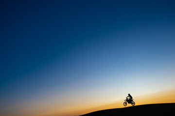 Fototapeta na wymiar Silhouette of motorcyclist at sunset jumping over dunes