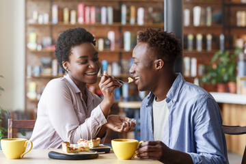 Beautiful black girl feeding yummy pie to her boyfriend at cozy cafe