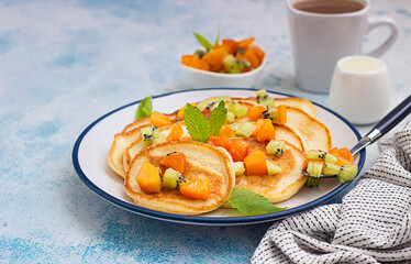 Homemade classic american pancakes with fruit salad made from apricot and kiwi. Healthy summer breakfast. Blue stone background.