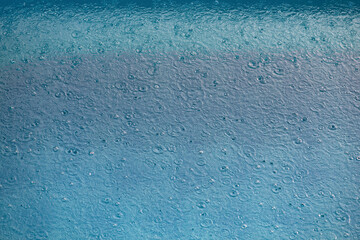 Drops of rain fall into the pool. Circles, bubbles and splashes on the surface of the water. Rain is watering. Water surface texture with drops. Top view