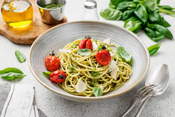 Pasta spaghetti with pesto sauce and fresh basil leaves in gray bowl. Light grey background