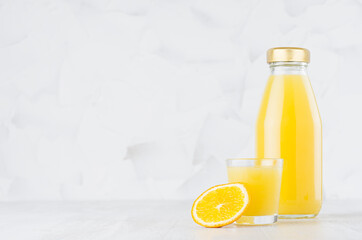 Fresh orange juice in glass bottle  mock up with wine glass, fruit slice on wood table in soft light white interior, template for packaging, advertising, design product, branding identity.