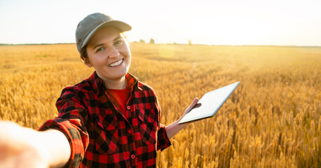 Woman farmer with digital tablet makes selfie on the background of a wheat field.
