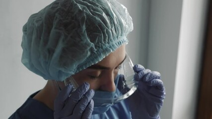 Tired nurse or doctor after taking a large number of patients due to the epidemic of coronavirus. In hat and face protective mask taking goggles and mask off over the hospital corridor.