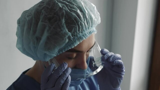 Tired nurse or doctor after taking a large number of patients due to the epidemic of coronavirus. In hat and face protective mask taking goggles and mask off over the hospital corridor.