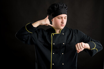 Obraz premium Young male dressed in a black chef suit showing it's time gesture