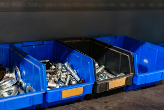 Galvanized steel bolts, screws, nuts in a blue plastic box on a rack in a warehouse.