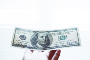 Hand with 100 dollar bill against a white bright background