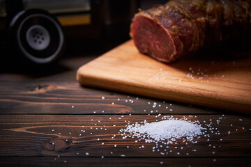 Large white smoked salt on an old black telephone cutting board on a dark wooden table close-up with shallow depth of field and blur.
