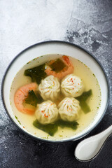 Bowl with panasian dumpling and prawn soup, vertical shot over black and white stone background