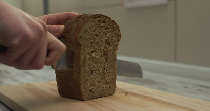 Woman's hands cut fresh loaf of bread with knife on wooden cutting board.