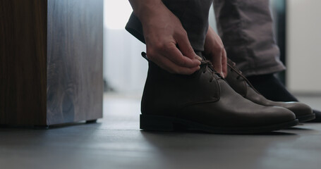 Young man put on his brown leather chukka boots indoor