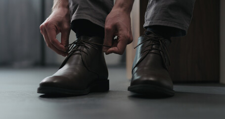 Young man put on his brown leather chukka boots indoor