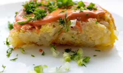 A portion of potato casserole with sauce and herbs on a white plate.The concept of healthy food
