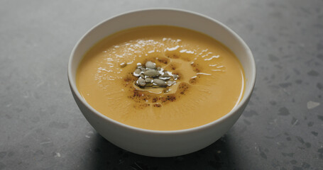 pumpkin cream soup in white bowl on terrazzo countertop