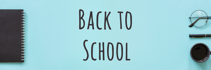 Back to school text and office supplies, stationery. Black color notepad, cup of coffee, spectacles and pen on blue background. Concept education. Flat lay Top view Banner