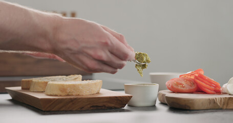 man spreading pesto on ciabatta bread slice on olive board