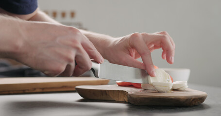 Fototapeta na wymiar man slicing mozzarella ball on olive wood board