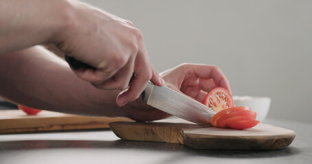 man slicing tomato on olive wood board