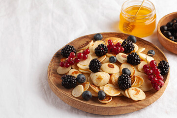 Tiny pancakes with berries and honey on a wooden plate. concept of Breakfast trends in the supply. Copy space