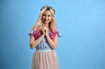 Blonde colored hair model smiling posing in studio on a blue background. Horizontal portrait of a cute caucasian young woman with a wreath on her head.
