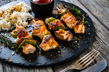 Grilled shashlik and white basmati rice on black stone plate on wooden table

