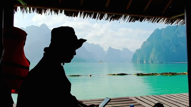 Silhouette young tourist woman sitting on bamboo raft house with limestone mountain background at cheow lan lake khao sok national park surat thani Thailand