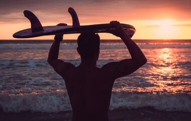 Backlit of a surfer holding his surfboard over his head looking at the sea during an amazing sunset