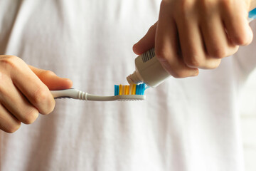 A young man holds a toothbrush and puts toothpaste on it