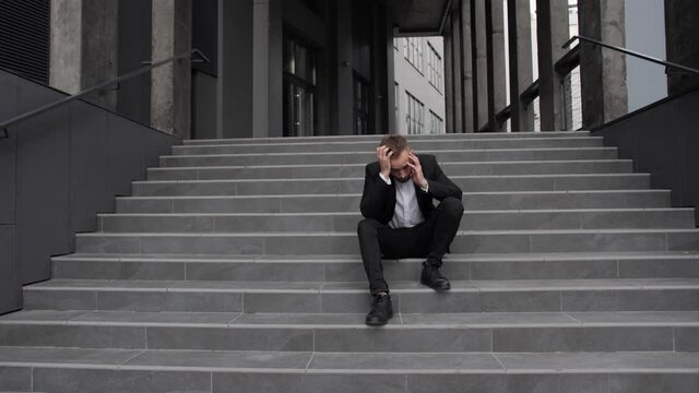 An fired office worker sits on the stairs and holds his head in crisis.