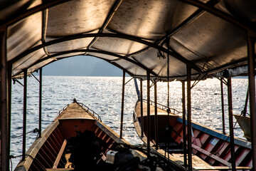 Fototapeta na wymiar Two empty long-tailed boats floating on the lake with rays of light in the morning. A look from the inside of vehicle to the lake and mountain. 