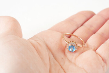 hand hold golden ring with big blue topaz and many diamonds on white background, gift concept