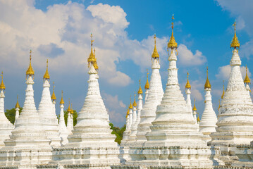 Fototapeta premium White stupas of the Sanda Muni pagoda against a cloudy blue sky. Mandalay, Myanmar