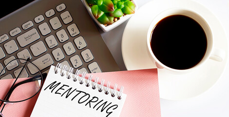 Office supplies, devices, coffee cup and glasses on white table with text MENTORING