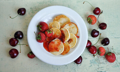 Homemade Mini pancakes and fresh strawberries, cherries on an old wooden table. Top view