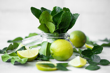 lime leaves in jar and ripe limes on a white table