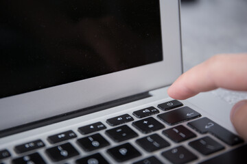 Pushing the power switch on a keyboard of a grey notebook with a finger by male hand