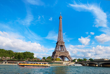 Fototapeta na wymiar Cityscape of Paris, France. Eiffel tower on a sunny day, with tourist boats on river Seine. Bright sunny day with feather clouds in blue sky.