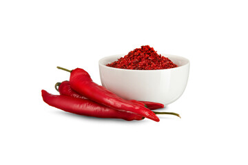 Red hot pepper flakes in white bowl and red peppers on white background.