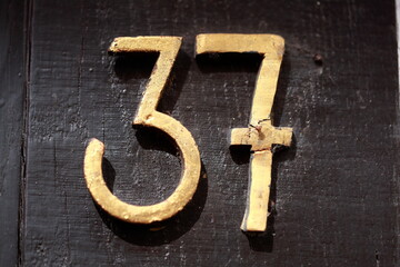 Goldenes Hausnummernschild Nummer Siebenunddreissig auf einem dunklen Holzbalken