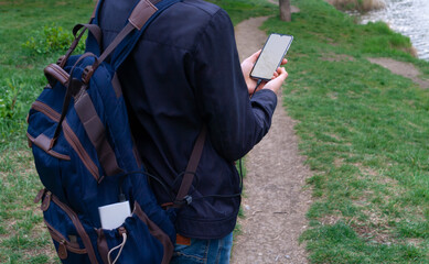 Man holding and using smartphone with blank white screen charges from the power bank in outdoor with nature background.