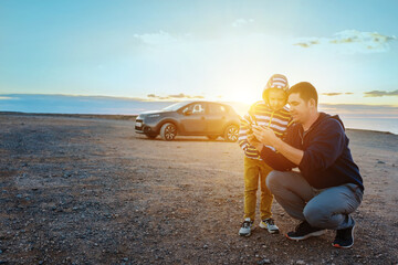 Father and son controlling fly drone on the seashore at sunset in summer day. Freedom, Family, Travel, Journey, Togetherness.