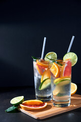 Health care, fitness, healthy nutrition diet concept. Fresh cool homemade citrus infused detox water with grapefruit, orange, lemon and lime and ice in glasses on dark background.