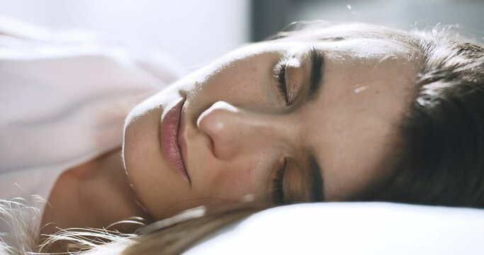 Close up of happy pretty Caucasian young woman lying on pillow and smiling cheerfully. Beautiful joyful girl waking up with smille in bedroom early in morning. Female portrait of sweet awakening.