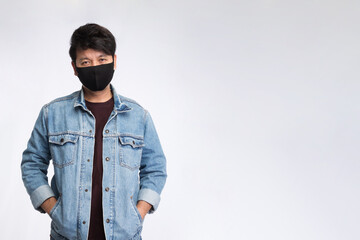 Asian man with face mask wear jacket jeans put the hand in pocket and look at camera, studio light portrait isolated on white background, COVID-19 concept