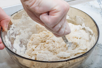 Thick dough is manually mixed in a transparent bowl.