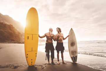 Happy friends surfing together on tropical ocean - Sporty people having fun during vacation surf day - Elderly and youth extreme sport lifestyle concept - obrazy, fototapety, plakaty