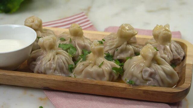 Close-up of delicious khinkali, dumplings poured with melted butter and sprinkled with fresh herbs. Khinkali on a wooden plate with sour cream. Khinkali on a marble background.