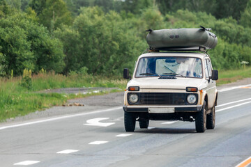 Old car jeep with a rubber boat on the roof rides on an asphalt road in the background forest landscape,. The concept of moving from city to city in your car. Traveling by car