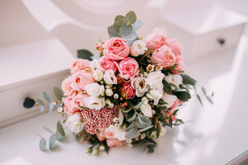 beautiful bouquet with pink roses, white flowers and green leaves of eucalyptus on a white table on a white background